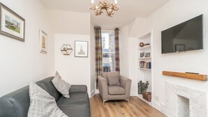 A living room with a black leather sofa, a grey armchair, a fireplace, a mounted TV, and a bookshelf. - Cosy Flat in Historic Old Town - Pass the Keys (Edinburgh)