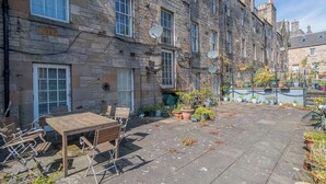 A stone building with multiple windows, a courtyard with a table and chairs, and potted plants. - Cosy Flat in Historic Old Town - Pass the Keys (Edinburgh)
