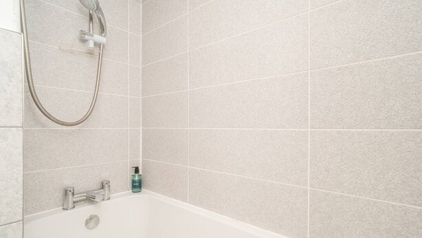 Une salle de bain avec une baignoire, une douchette à main et un flacon de shampoing.