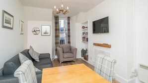 A modern living room with a sofa, armchair, wooden table, and a TV mounted on the wall. - Cosy Flat in Historic Old Town - Pass the Keys (Edinburgh)