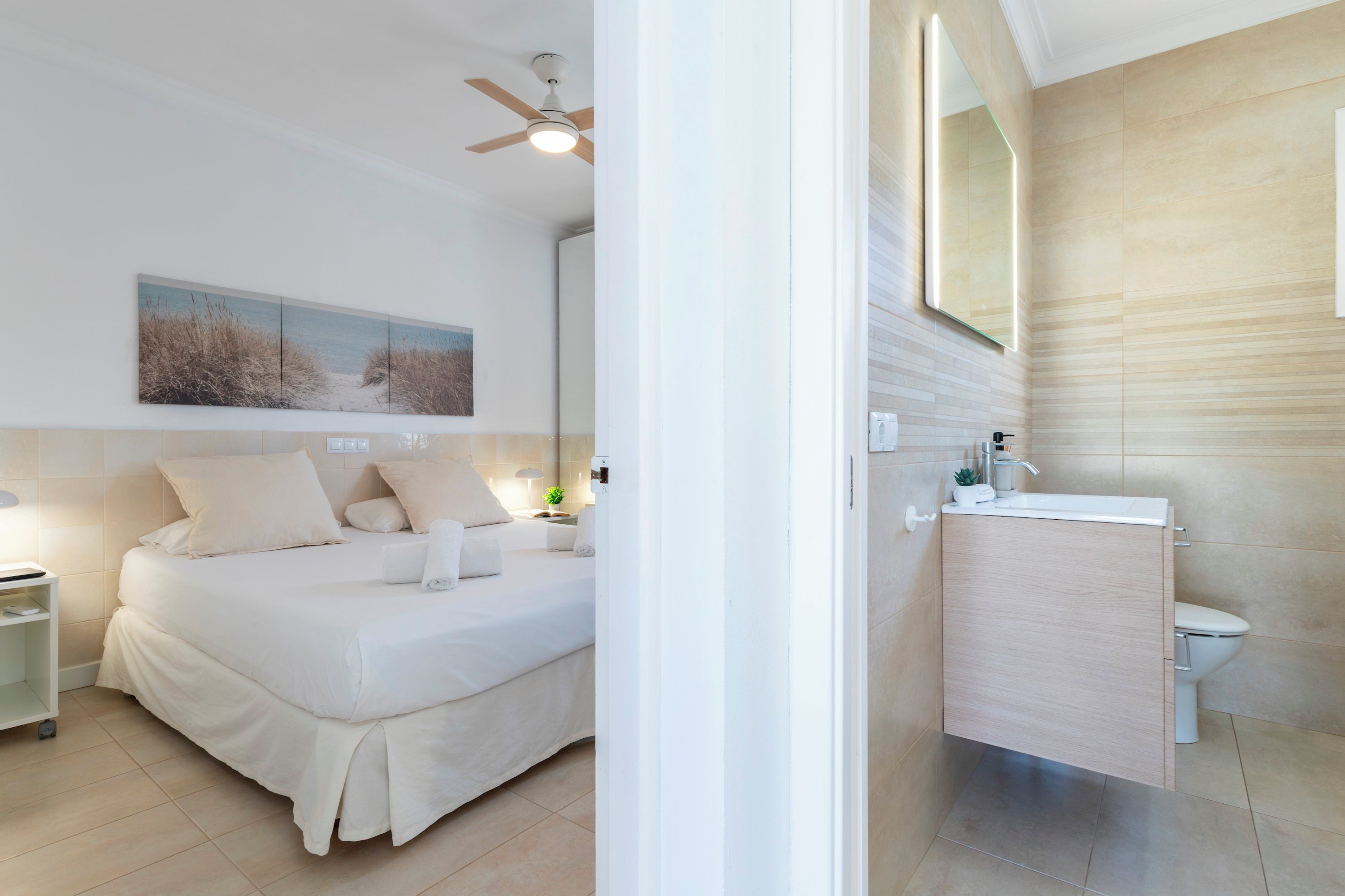 A bedroom with a bed, a bedside table, a nightstand, a ceiling fan, and a wall-mounted painting.