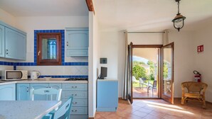 Een keuken met blauwe kastjes, een magnetron en een fornuis. Er is een eethoek met een tafel en stoelen.