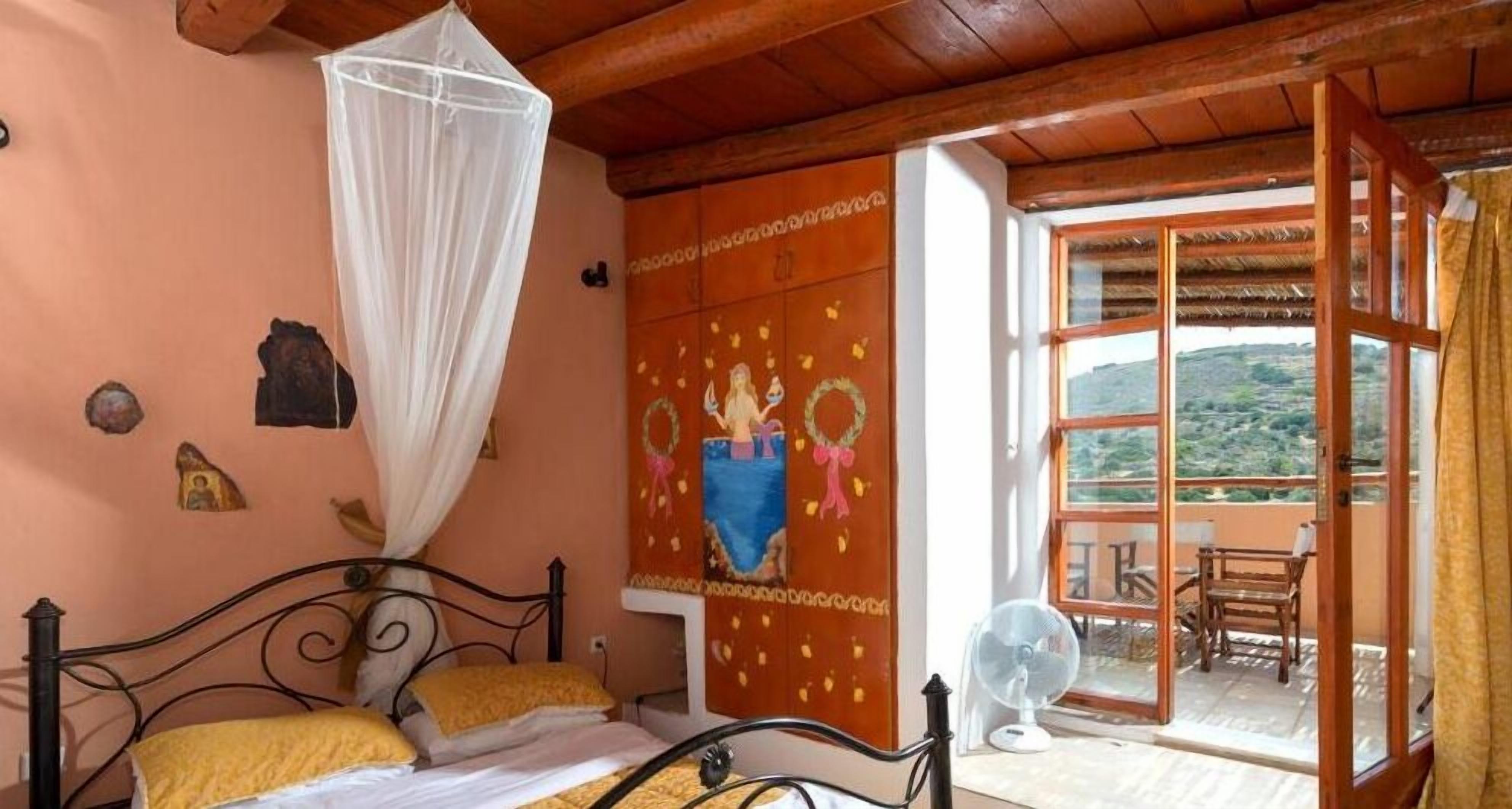 A bedroom with a bed, a bedside fan, a mosquito net, and a view of the outdoors.