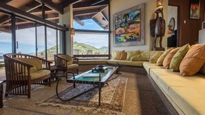 Un amplio salón con un gran ventanal que ofrece vistas a las colinas, un sofá con cojines y una mesa de centro.