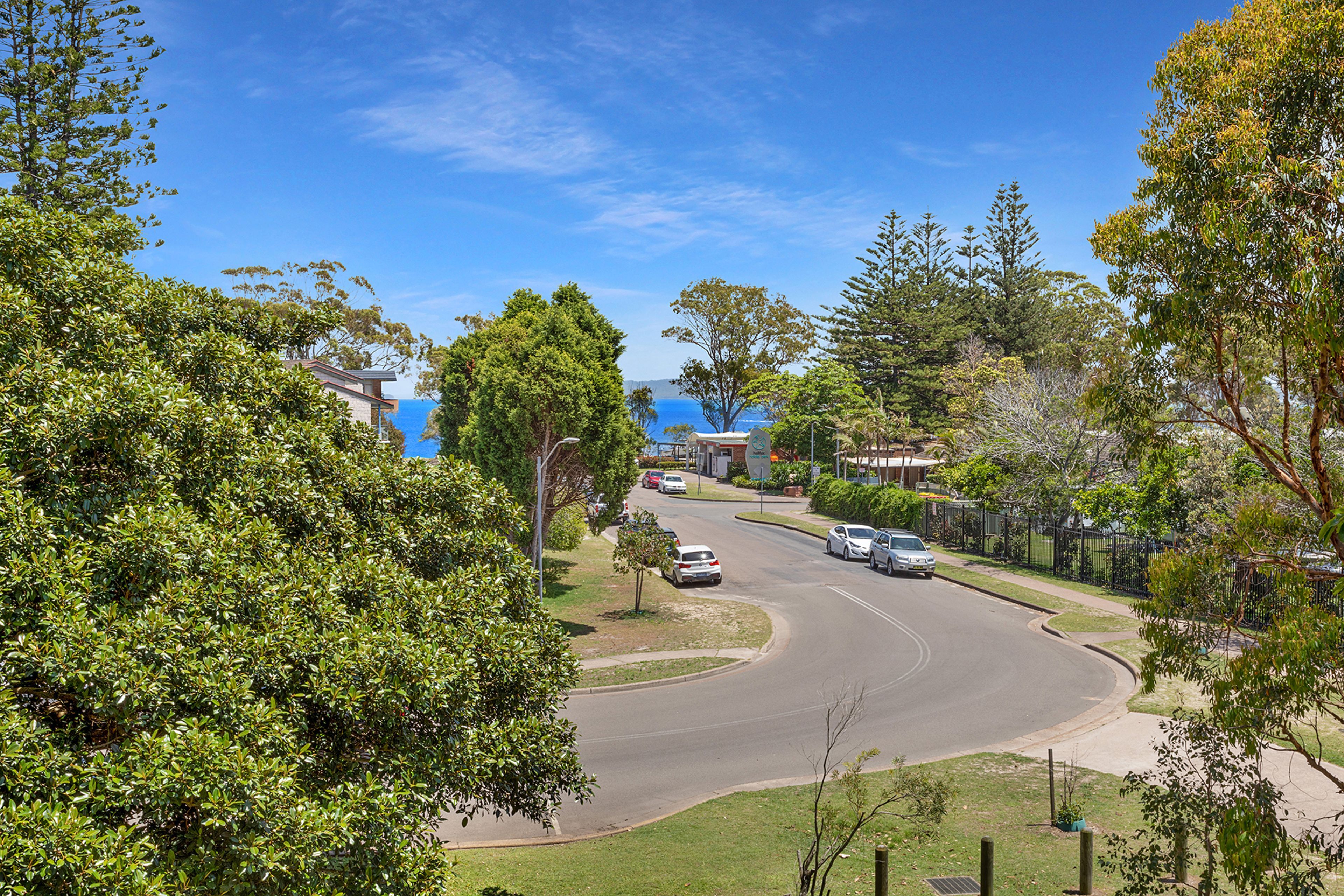 A residential street with houses, cars, and a clear view of the sea.
