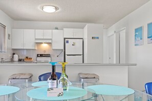A modern kitchen with white cabinets, a refrigerator, and a dining table with blue placemats.