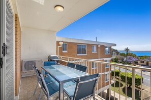 Een balkon met een tafel en stoelen, met uitzicht op een woongebied en de zee.