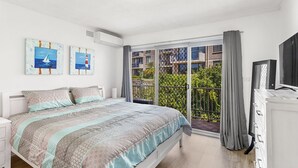 A bedroom with a bed, a TV, and a balcony with a view of buildings and greenery. - Yarramundi a Nelson Bay Apartment Near Beach (Nelson Bay)