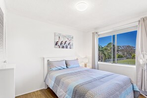 A bedroom with a bed, a painting, a window with curtains, and a fan.