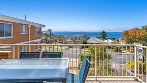 A balcony with a table and chairs, overlooking a residential area with houses and a clear view of the ocean. - Yarramundi a Nelson Bay Apartment Near Beach (Nelson Bay)