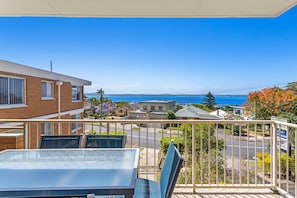 Een balkon met een tafel en stoelen, met uitzicht op een woonwijk met huizen en een helder uitzicht op de oceaan.