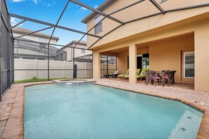 A swimming pool with a covered patio area, outdoor furniture, and a view of neighboring houses. - Disney near Resort Retreat 6BR w Pool & Theme Room (Kissimmee)