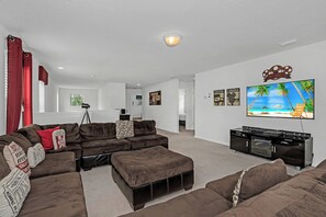 A living room with a sectional sofa, a flat-screen TV, and a fireplace. - Disney near Resort Retreat 6BR w Pool & Theme Room (Kissimmee)