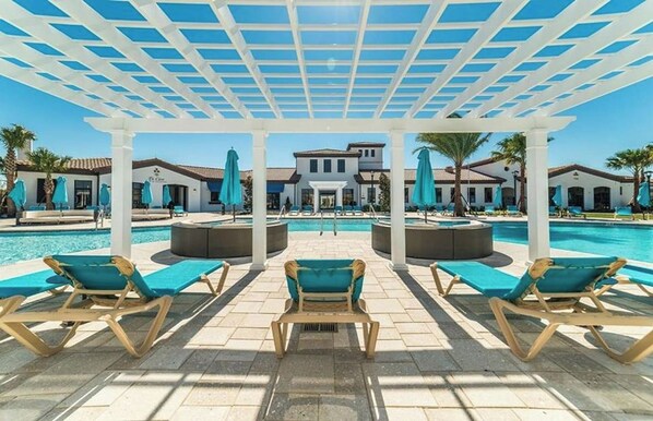 A poolside area with lounge chairs and umbrellas, a covered seating area, and a building in the background.