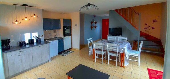 A modern kitchen with a dining area, a TV, and a staircase. - Gite*** 6/8 persons n°474 (Anzême)