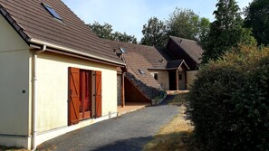 A residential building with a sloped roof, a covered porch, and a gravel driveway. - Gite*** 6/8 persons n°474 (Anzême)