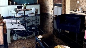 A modern kitchen with white cabinets, a dining area with a glass table, and a blue chair. - Siracusa villa Gavetta (SIRACUSA)