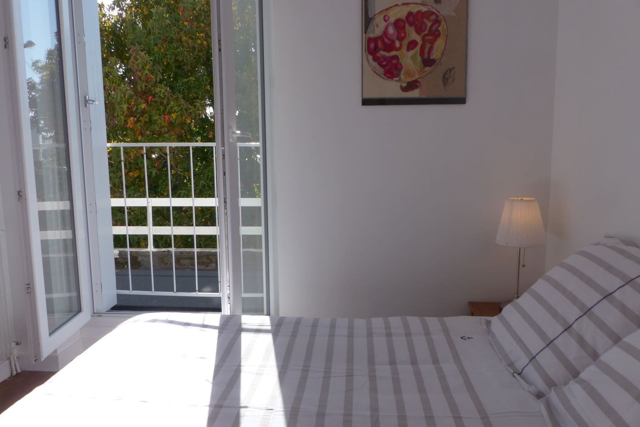 A bedroom with a bed, a nightstand, a lamp, a door leading to a balcony, and a painting on the wall.