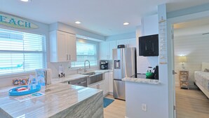 A modern kitchen with a marble countertop, stainless steel appliances, and a view of the adjacent bedroom. - Haven cottage Across street from beach  and  Heated Pool (Siesta Key)
