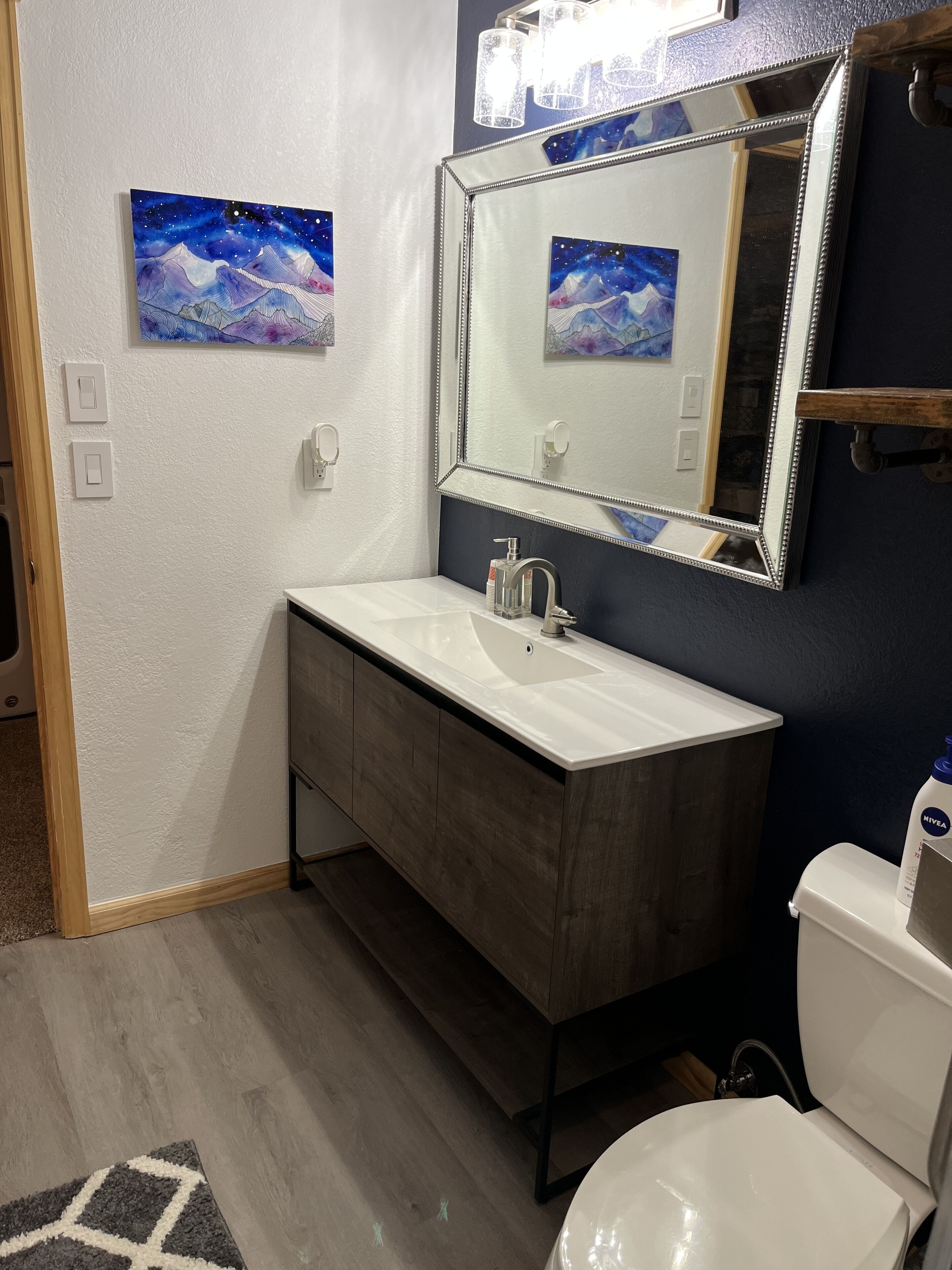 Un baño con un lavamanos blanco, tocador de madera oscura, un espejo grande y un inodoro blanco.