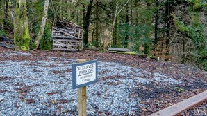A 'RESERVED PARKING' sign for 'Invernahyle Cottage' in a forested area with gravel ground. - 3 bedroom accommodation in Duror (Duror)