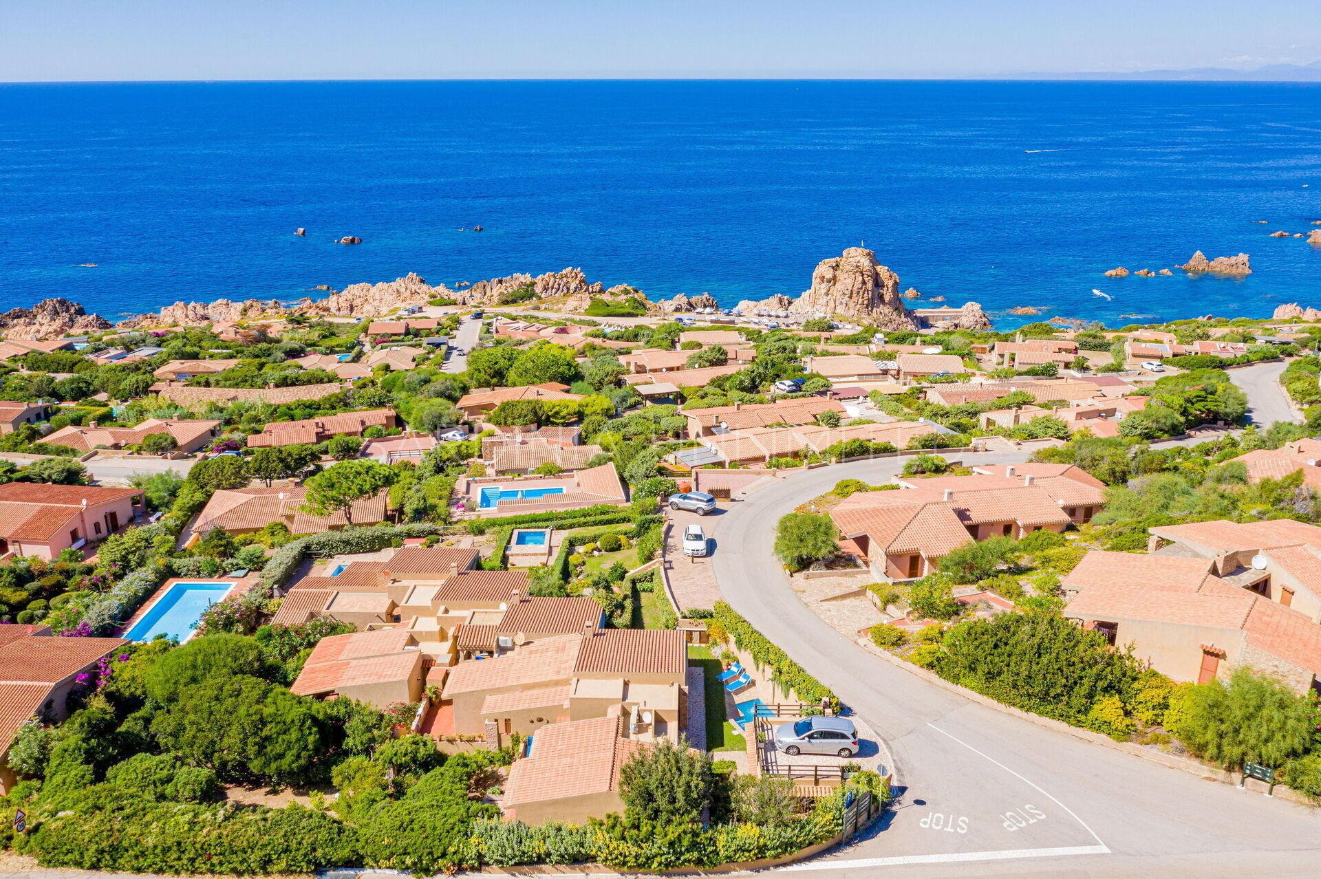 A coastal residential area with houses, a winding road, and a clear view of the sea.