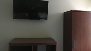 A room with a flat-screen TV mounted on the wall, a wooden cabinet, and a small table. - Magna Hotel (Jamaica)