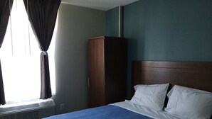 A hotel room with a bed, a wardrobe, and an air conditioning unit. - Magna Hotel (Jamaica)