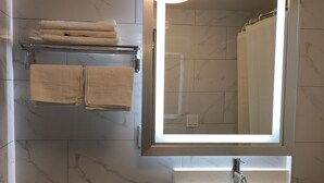 A modern bathroom with a toilet, a sink, a mirror, and a towel rack. - Magna Hotel (Jamaica)