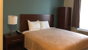 A hotel room with a bed, a nightstand, a lamp, a wardrobe, and a window with curtains. - Magna Hotel (Jamaica)