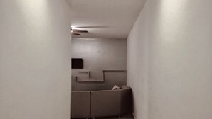 Ein enger Korridor mit Holzboden führt zu einem Raum, der eine Couch und einen an der Wand befestigten Flachbildfernseher beherbergt.
