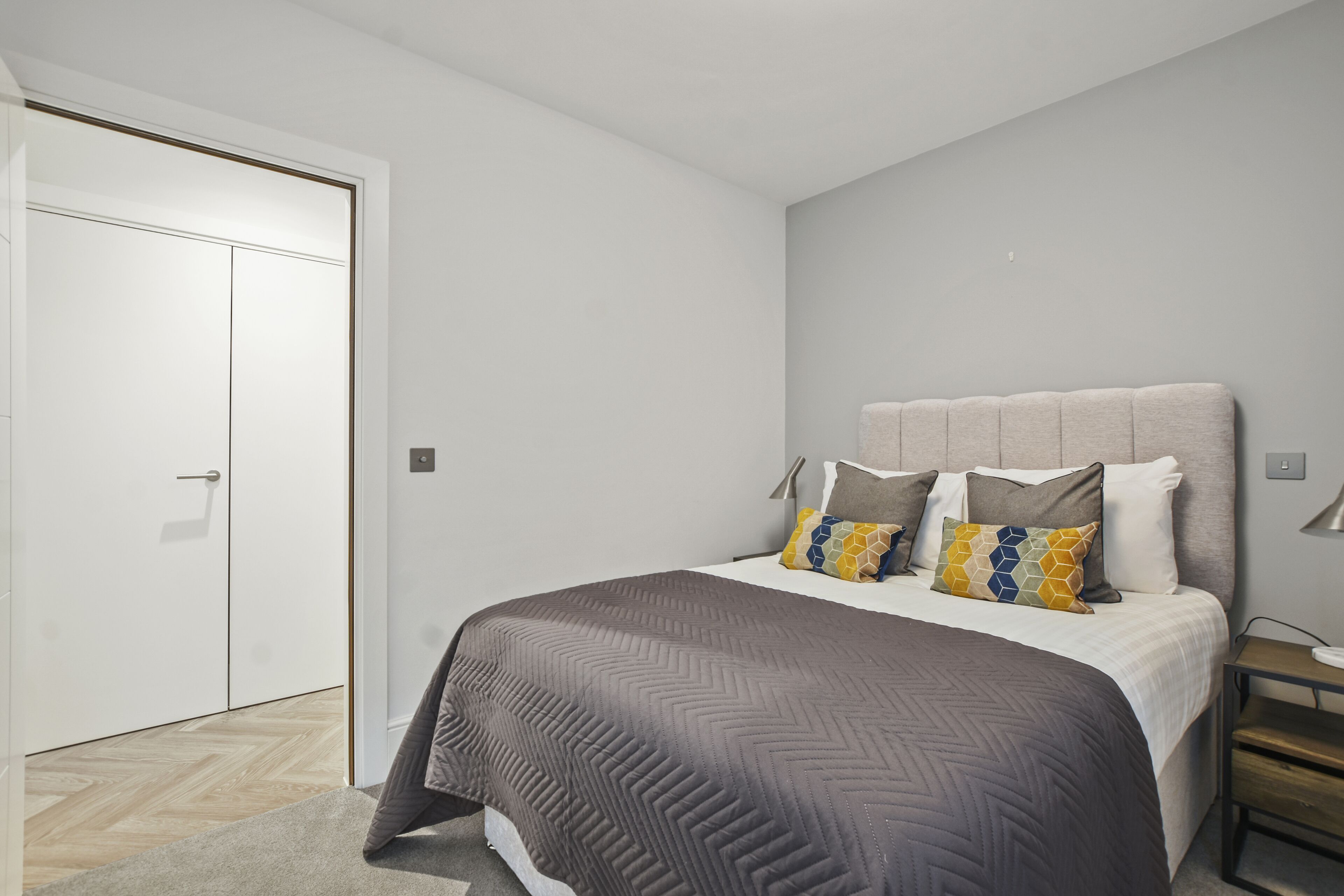 A bedroom with a bed, bedside tables, a wardrobe, and a door.