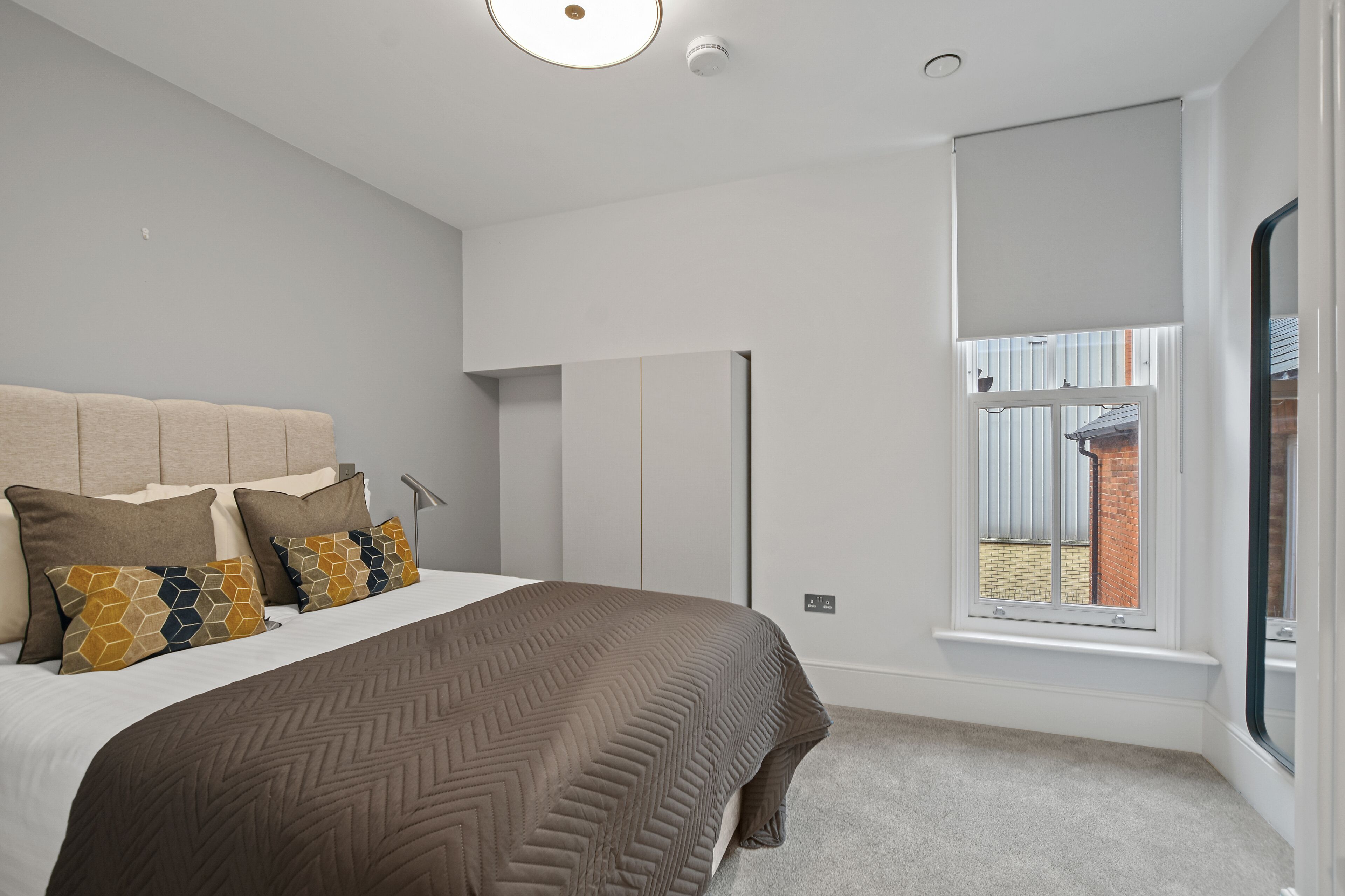 A bedroom with a bed, pillows, a wardrobe, and a window with a view.