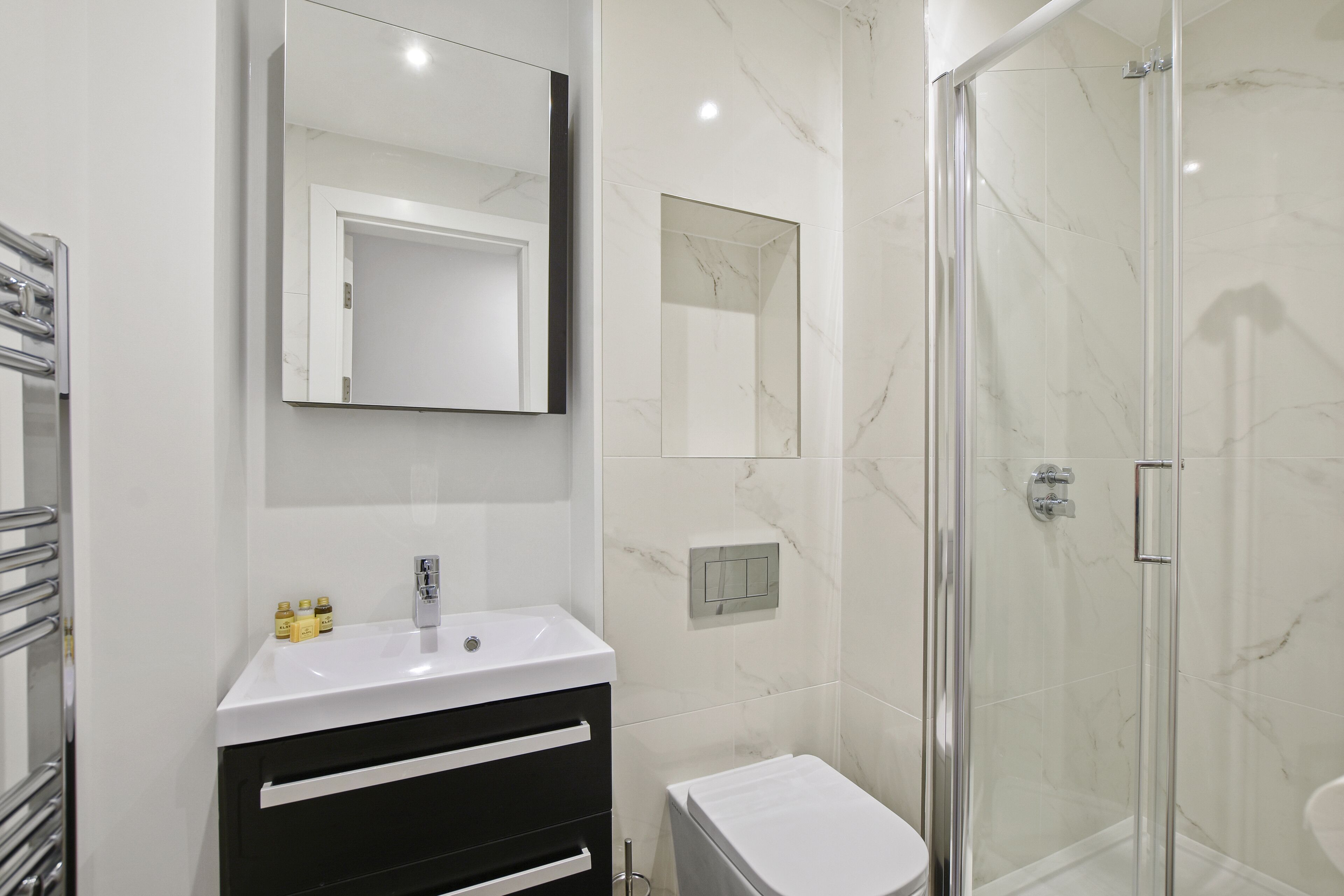 A modern bathroom with a white sink, black vanity, a glass shower enclosure, and a large mirror.