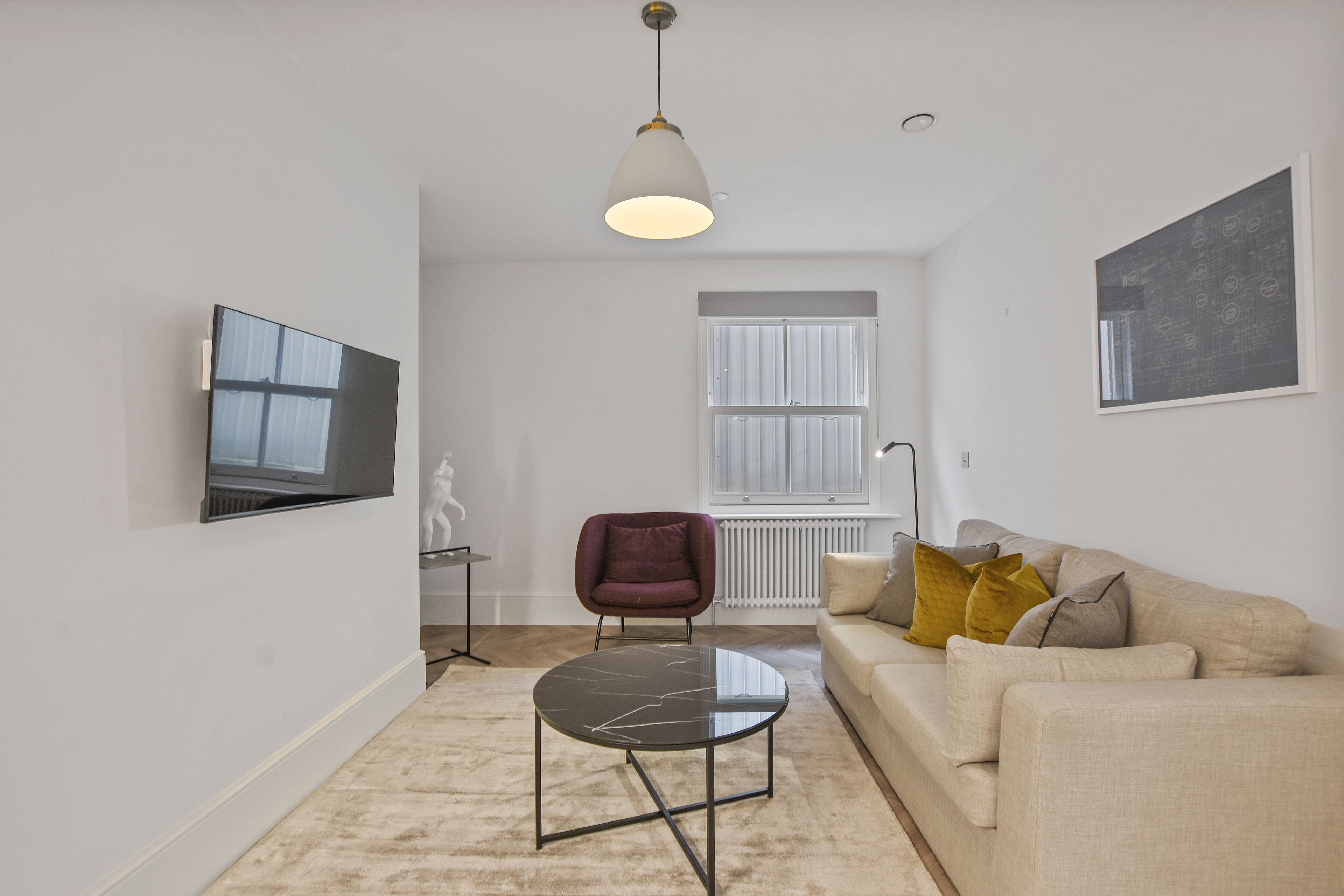 A modern living room with a beige sofa, a round coffee table, a purple armchair, and a large window with blinds.
