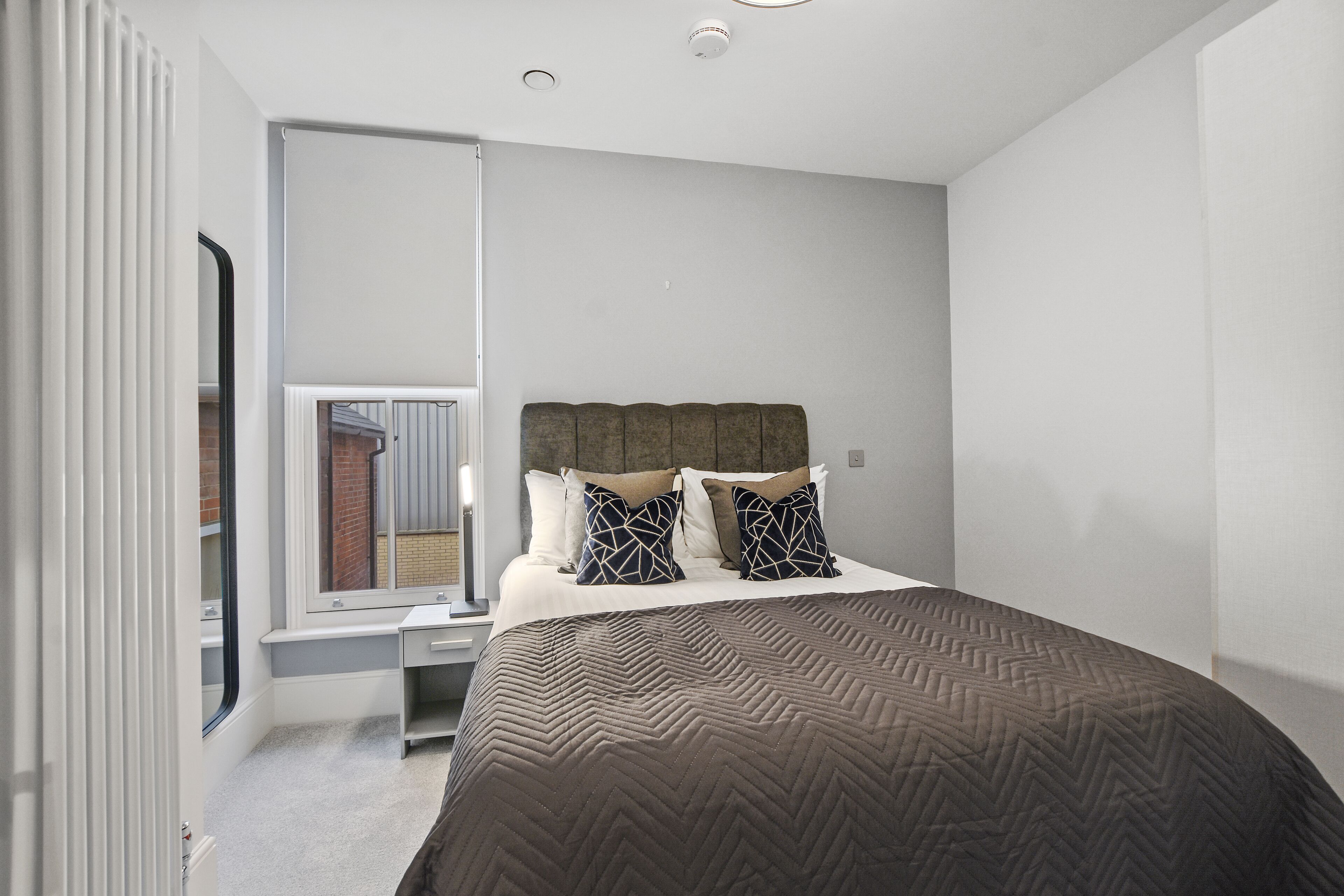Ein Schlafzimmer mit einem großen Bett, einem Fenster mit Blick auf ein Ziegelgebäude und einem Schreibtisch mit Stuhl.