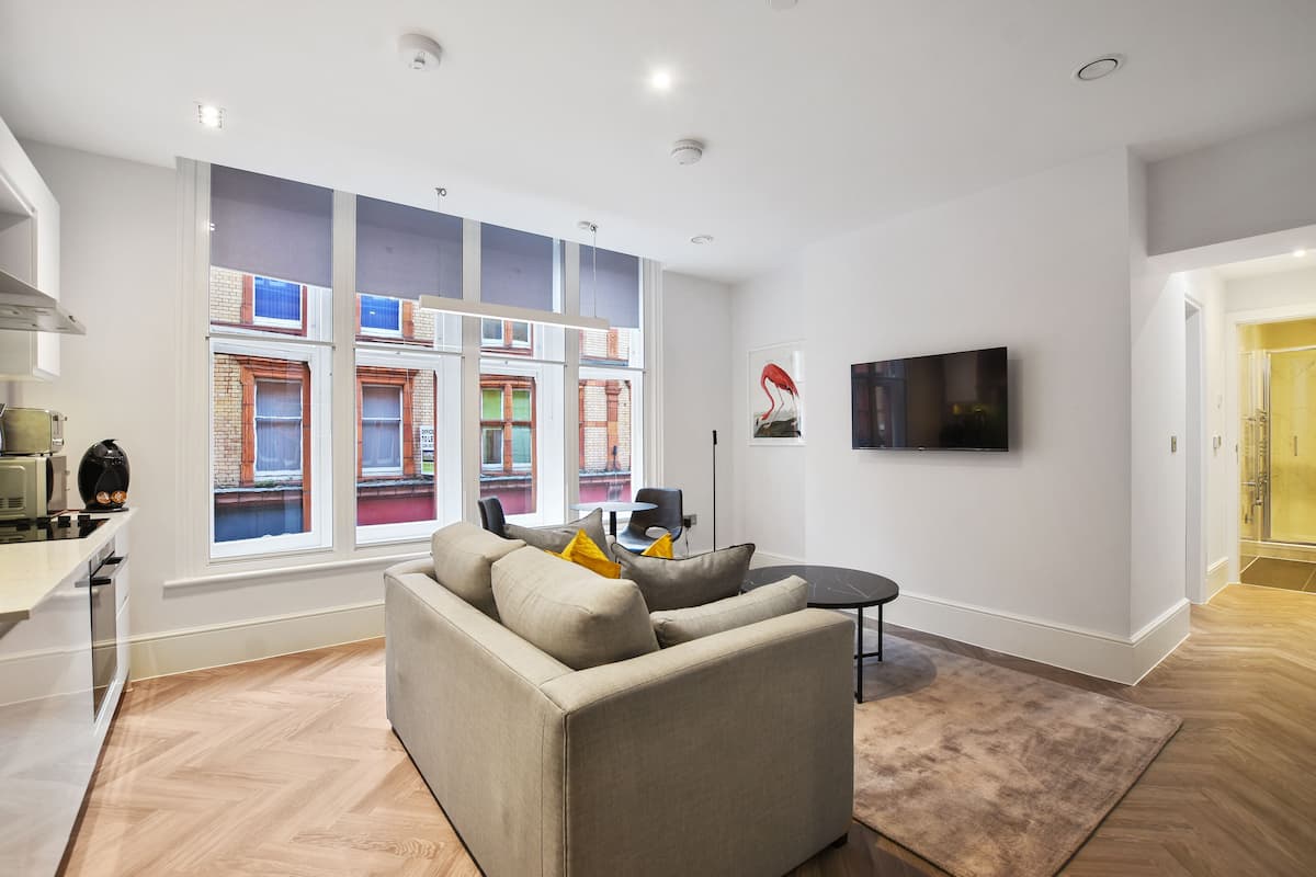 A modern living room with a sofa, a flat-screen TV, and a large window with a view of buildings.