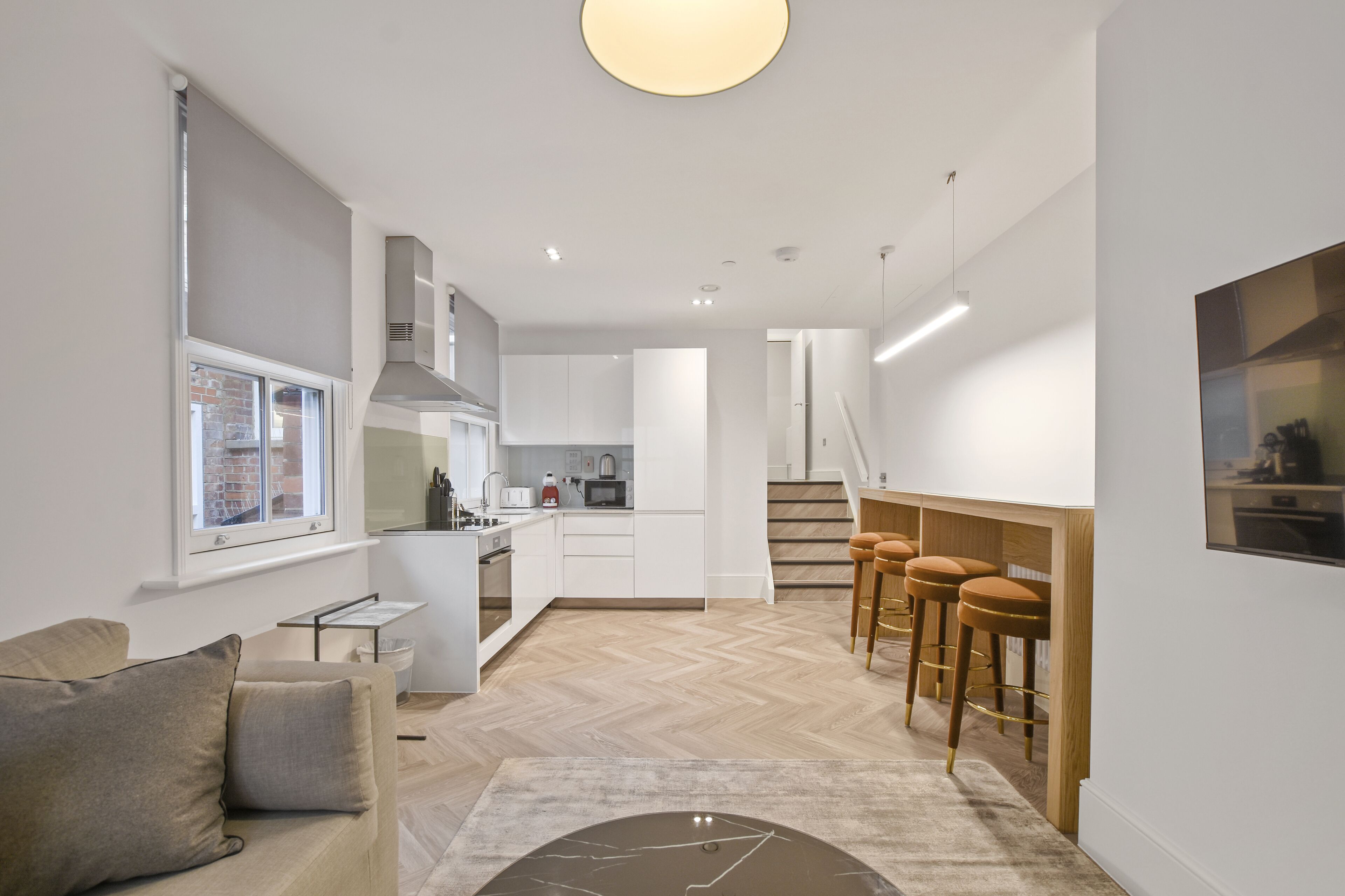 Una cocina moderna con armarios blancos, piso de espiga y una barra con taburetes.