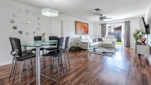 Un salon moderne avec une table à manger en verre, des chaises noires, un canapé blanc et un ventilateur de plafond.