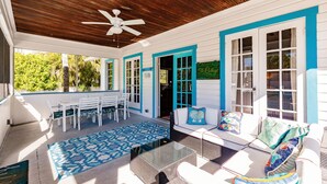 A covered outdoor area with a ceiling fan, white and blue furniture, and a patterned rug. - Vintage Cottage from 1936 across street from Beach  and  Heated Pool (Siesta Key)