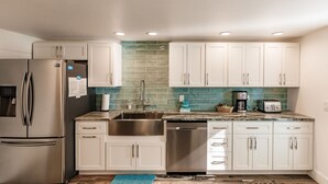 A modern kitchen with white cabinets, stainless steel appliances, and a green tiled backsplash. - Vintage Cottage from 1936 across street from Beach  and  Heated Pool (Siesta Key)