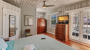 A bedroom with a bed, a dresser, a television, and a window with a view. - Vintage Cottage from 1936 across street from Beach  and  Heated Pool (Siesta Key)