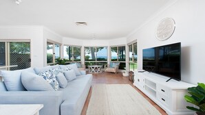 A spacious living room with a large TV, a light blue sofa, and a view of the outdoors.