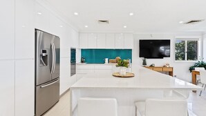 A modern kitchen with white cabinetry, a stainless steel refrigerator, a teal backsplash, and a flat-screen TV mounted on the wall.