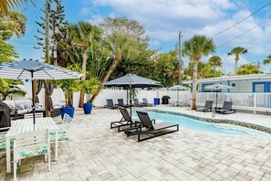 Relax by the pool surrounded by lush greenery and palm trees, with lounge chairs and umbrellas providing shade.