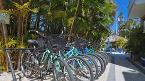 A row of bicycles parked in a shaded area with palm trees and a building in the background. - Nook Cottage Across street from beach  and  Heated Pool (Siesta Key)