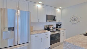 A modern kitchen with white cabinets, stainless steel appliances, a microwave, and a coffee maker. - Nook Cottage Across street from beach  and  Heated Pool (Siesta Key)