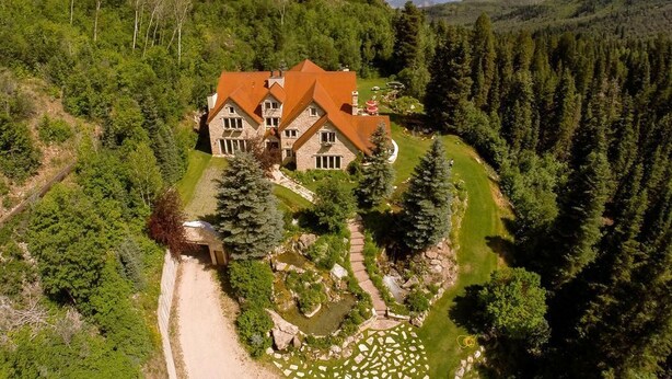 Ein großes, mehrgeschossiges Haus, umgeben von dichtem Wald, mit einem gepflegten Garten und einem klaren Weg zum Eingang.