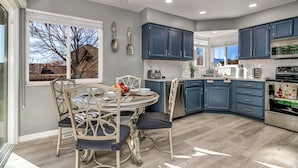A modern kitchen with blue cabinets, a dining table with chairs, and a view of the outdoors. - Spacious Modern Gorgeous Mountain Views Fort Carson Fire Pit!  (Colorado Springs)