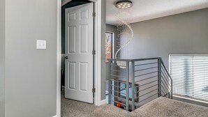 A hallway with a white door, a staircase with a metal railing, and a ceiling light fixture. - Spacious Modern Gorgeous Mountain Views Fort Carson Fire Pit!  (Colorado Springs)